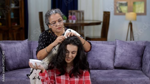 A caring Indian grandma is oiling her sweet granddaughter's hair with natural oil - dry skull  winter season  healthy hair  strong roots  home remedy  hot oil massage. A young college student with ...