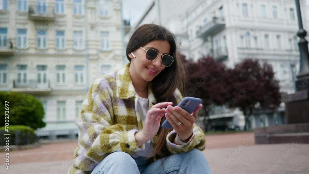 A smiling female student browsing the news feed on her smartphone while sitting in the park. A female co-worker browsing the web, browsing emails during a break in the street. Young girl sitting on A smiling female student browsing the news feed on her smartphone while sitting in the park. A female co-worker browsing the web, browsing emails during a break in the street. Young girl sitting on