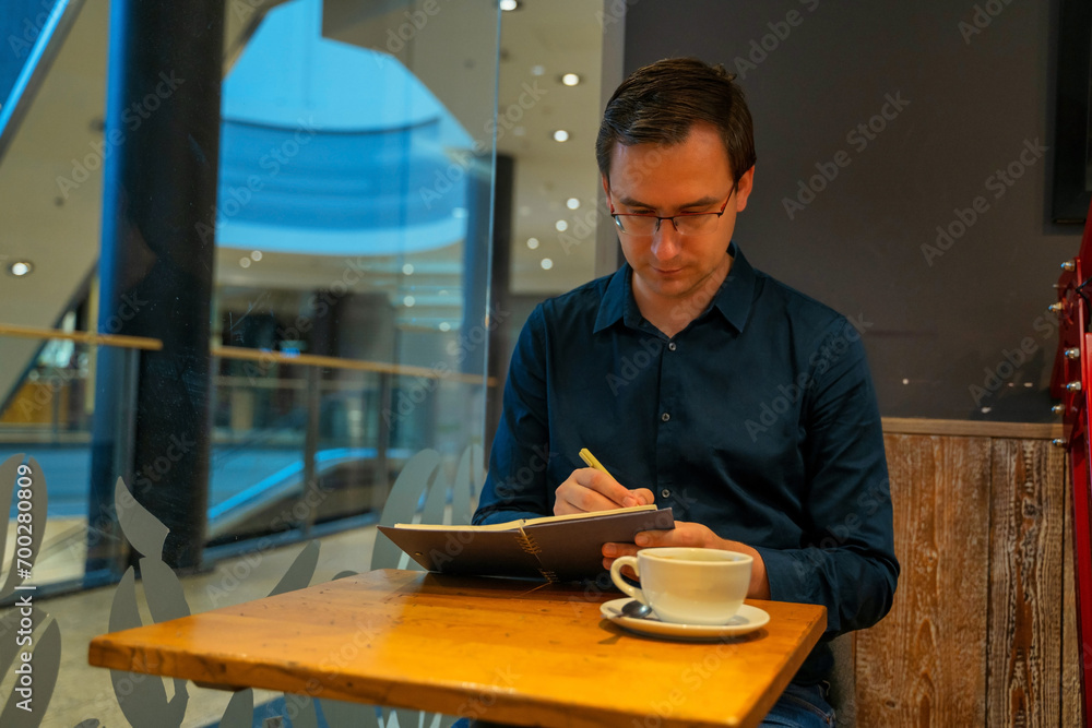 Thoughtful mature adult business man writing in notebook, middle aged author or writer taking notes thinking of new ideas, mature male student making checklist, learning in cafe sitting at table.