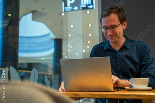 Obraz na płótnie A man in shirt working on laptop inside a cafe with a coffee, business man working remotely concept w salonie
