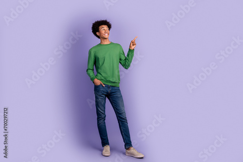Full length photo of good mood positive guy wear green pullover showing finger looking empty space isolated purple color background