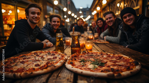 Relaxed friends sitting at table at party. Young people in casual clothes sitting on terrace roof, talking, eating pizza and drinking wine. Communication, friendship concept