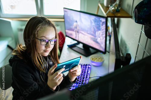 Focused Girl Playing a Mobile Game with Gaming Setup in the Background
