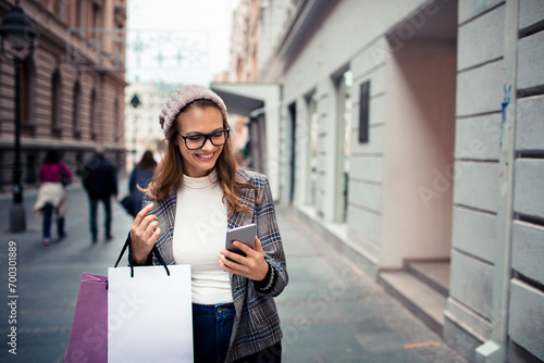 Young stylish woman using smartphone while shopping in city photo