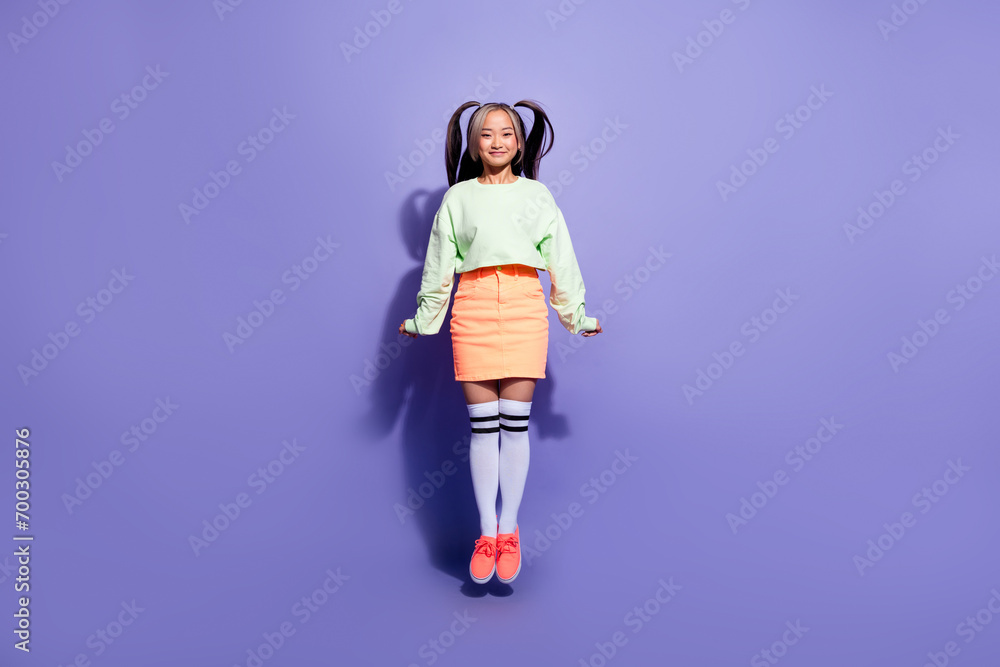 Full body photo of funky girl jumping trampoline wearing green stylish jumper with peachy mini skirt isolated on purple color background Full body photo of funky girl jumping trampoline wearing green stylish jumper with peachy mini skirt isolated on purple color background