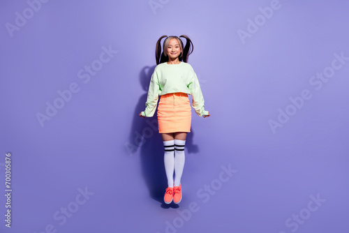 Full body photo of funky girl jumping trampoline wearing green stylish jumper with peachy mini skirt isolated on purple color background