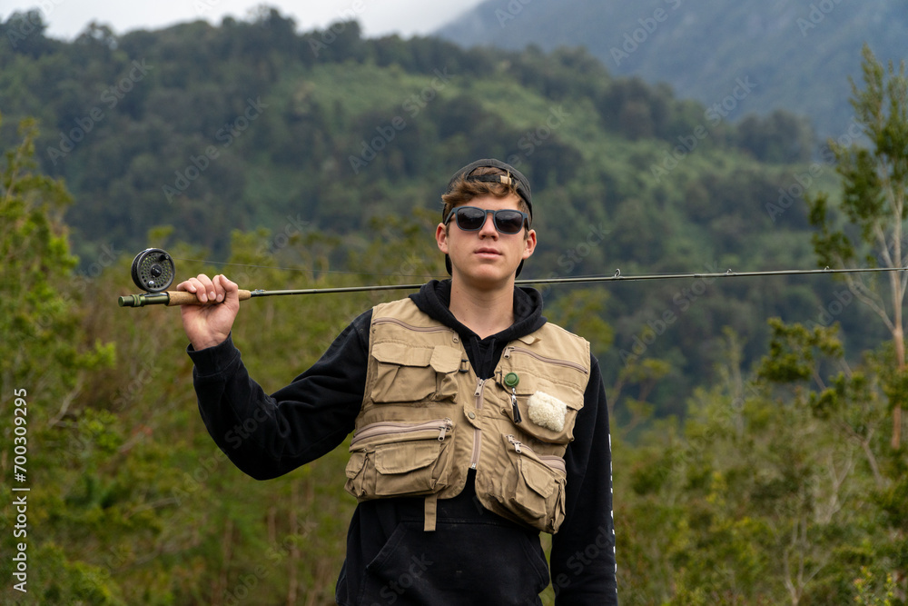 Fototapeta premium Young man with fishing gear and rod looking at camera