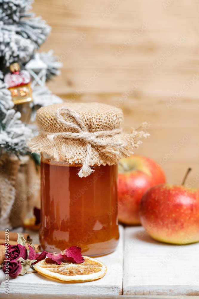 Jar of honey, apples and dry orange slices on wooden table.
