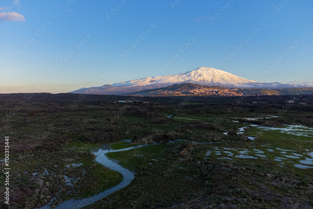 Bronte town under the snowy and majestic volcano Etna and a cloudy blue sky
