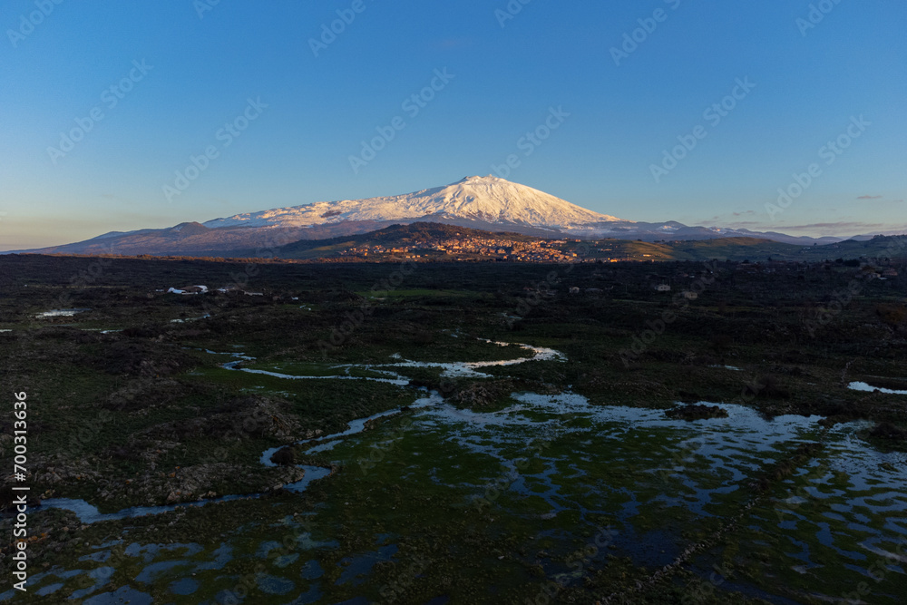 Fototapeta premium Bronte town under the snowy and majestic volcano Etna and a cloudy blue sky