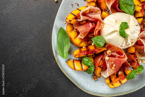 Heathy summer salad with grilled peach, ham and burrata on a dark background. top view. copy space for text photo