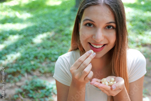 Close-up of healthy girl eating macadamia nuts in the park. Looks at camera. photo