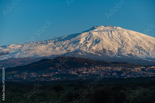 Bronte town under the snowy and majestic volcano Etna and a cloudy blue sky