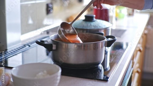 Caucasian Woman Stirring Tomato Soup Cooked in Metal Pot on Kitchen Stove Cooker