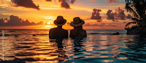 Couple in hats enjoys sunset poolside during vacation. © TheWaterMeloonProjec