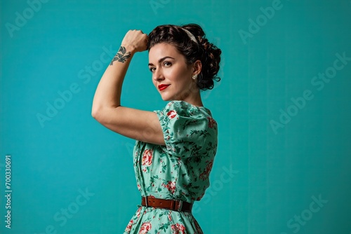 Confident young woman in retro dress showing her power with hand gesture. Feminism, girl power and can-do attitude. We can do it! Rosie the Riveter concept