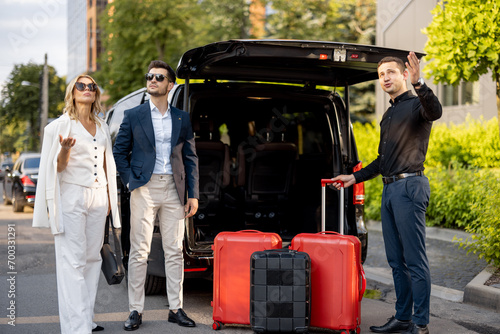 Business couple standing by a minivan taxi waiting for their chauffeur or porter to help them with a suitcases. Concept of business trips and travel photo