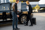 Chauffeur helps businessman with a suitcase to get in the car, opening a door of a luxury black taxi. Man having a business trip