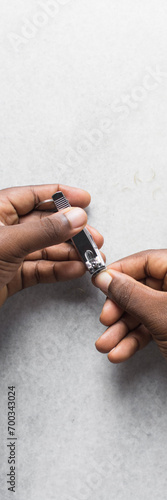 Overhead view of cutting nails with silver nail clippers, top view of manicure on brown skin hands, process of cutting short nails