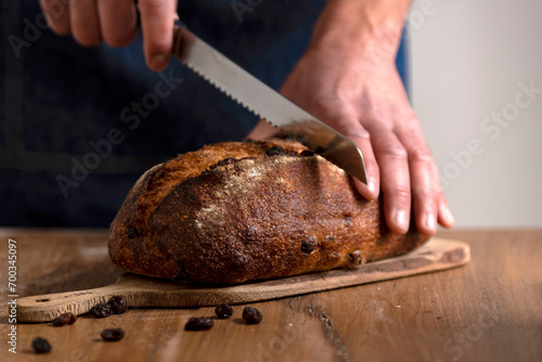 hands holding big homemade sourdough bread with seeds and cereals and bread knife cutting into slices photo