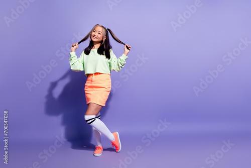 Full size photo of pretty korean girl with ponytails hairdo wear oversize pullover hold two hair tails isolated on violet color background