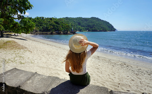 Holidays in Brazil. Back view of traveler girl sitting on wall in Ubatuba beach, Brazil. photo
