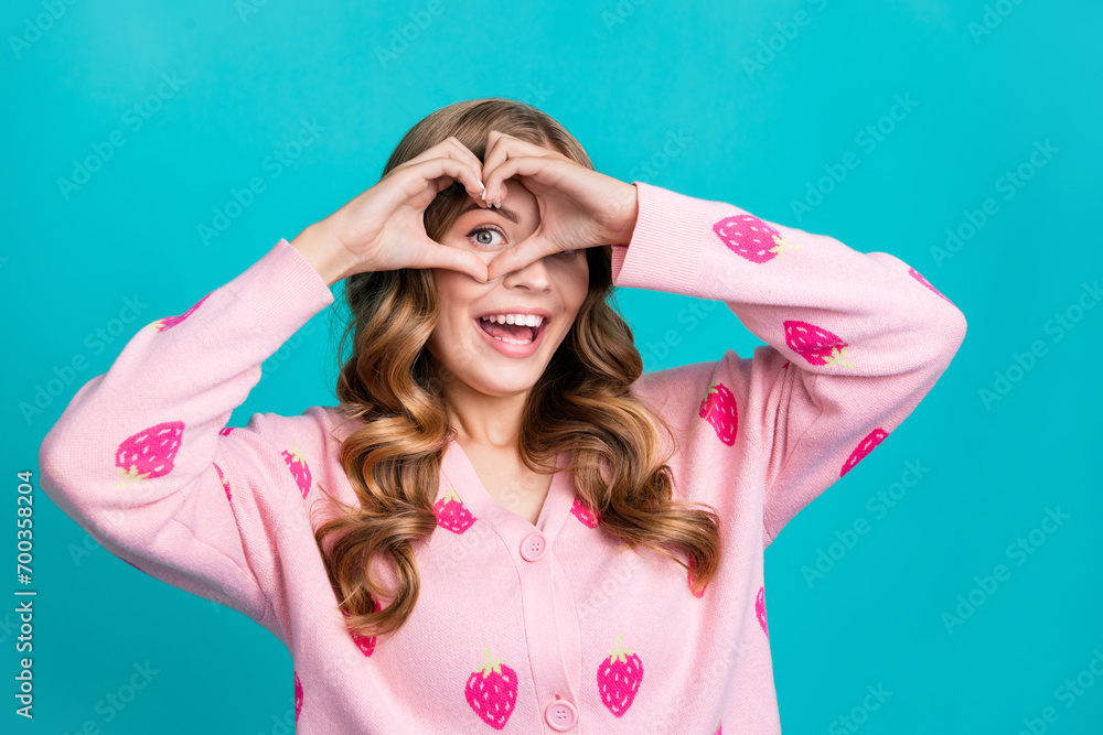 Portrait of young adorable stunning woman in stylish glamour pink cardigan show heart symbol on eye isolated over blue color background Portrait of young adorable stunning woman in stylish glamour pink cardigan show heart symbol on eye isolated over blue color background