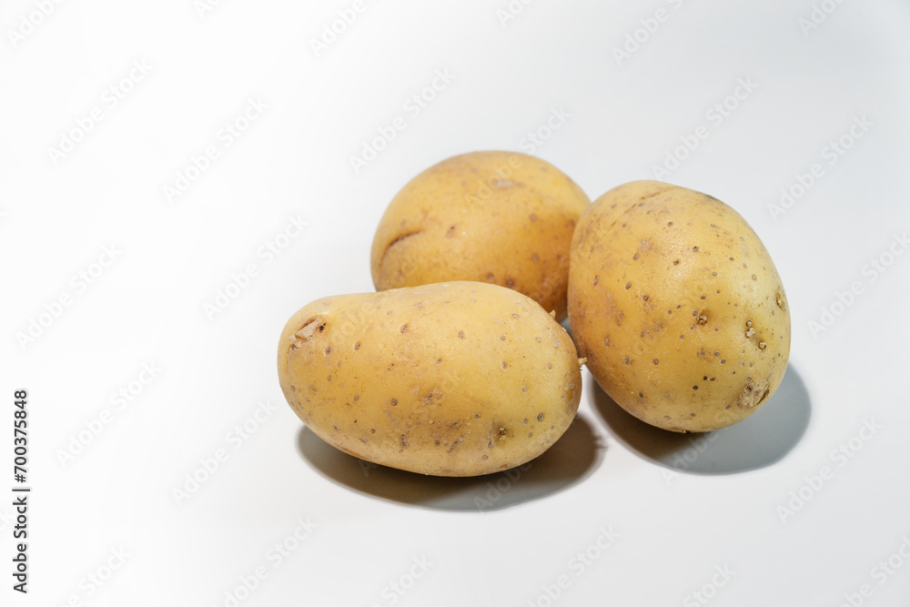Three raw potatoes on a light gray background, carbohydrate-containing root vegetable and staple food in many parts of the world, copy space, selected focus Three raw potatoes on a light gray background, carbohydrate-containing root vegetable and staple food in many parts of the world, copy space, selected focus