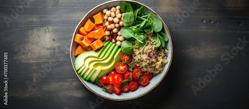 Vegan lunch bowl with avocado, quinoa, sweet potato, tomato, spinach, and chickpea vegetable salad, seen from above.