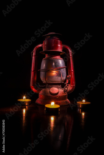 Horizontal Color Image of an antique lantern, light painted with four votive candles surrounding it. 