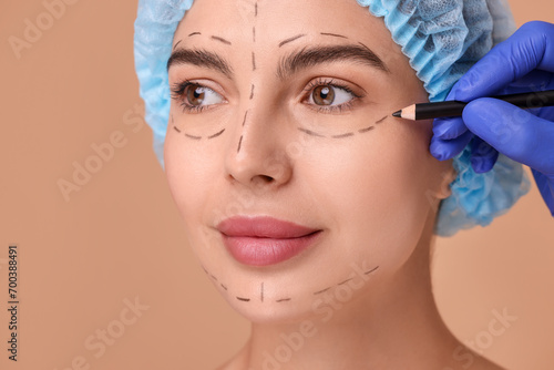 Fotografi Doctor drawing marks on woman's face for cosmetic surgery operation against beig