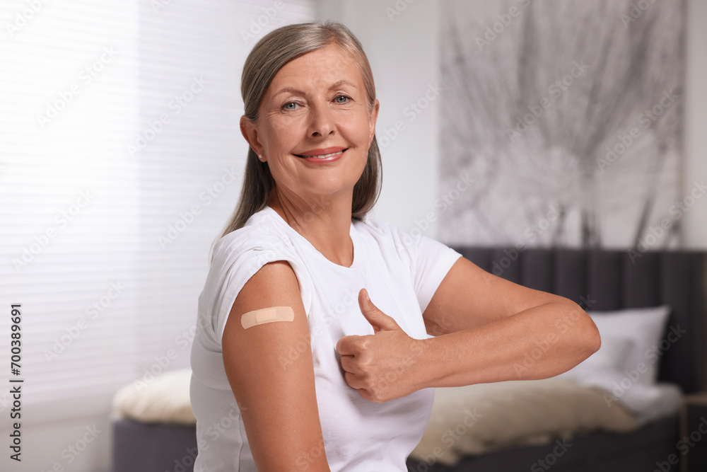Senior woman with adhesive bandage on her arm after vaccination showing thumb up indoors Senior woman with adhesive bandage on her arm after vaccination showing thumb up indoors