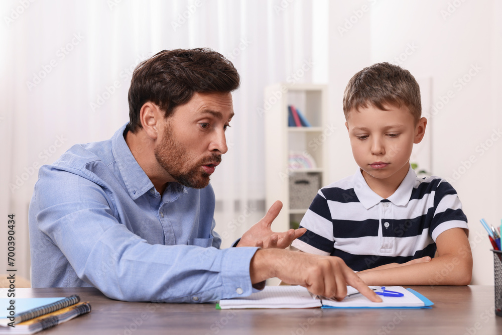 Son studying with annoyed father at table in room. Suffering from dyslexia Son studying with annoyed father at table in room. Suffering from dyslexia