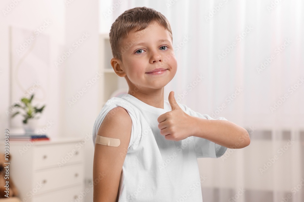 Boy with sticking plaster on arm after vaccination showing thumbs up indoors Boy with sticking plaster on arm after vaccination showing thumbs up indoors