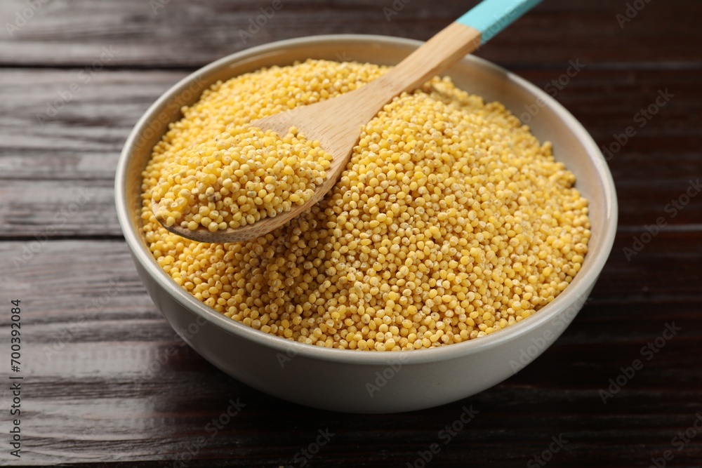 Millet groats in bowl and spoon on wooden table, closeup Millet groats in bowl and spoon on wooden table, closeup