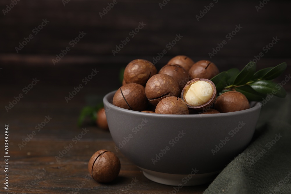 Tasty Macadamia nuts and green twig in bowl on wooden table. Space for text Tasty Macadamia nuts and green twig in bowl on wooden table. Space for text
