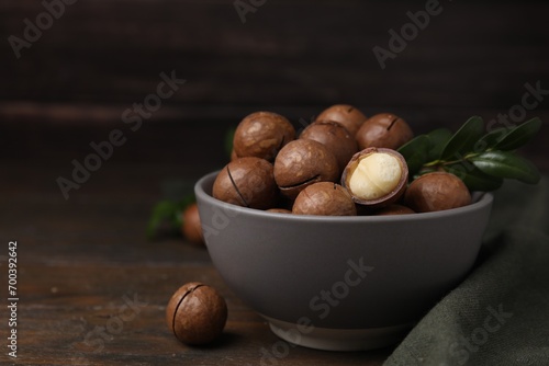 Tasty Macadamia nuts and green twig in bowl on wooden table. Space for text