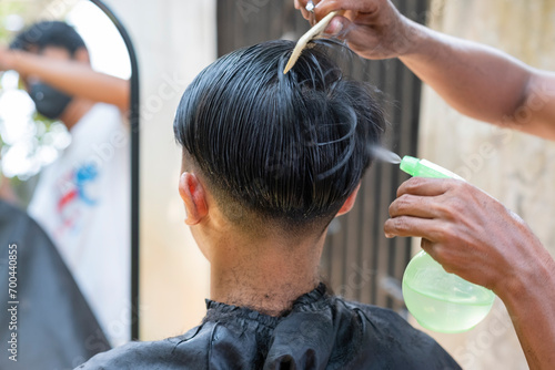 A hairdresser is spraying water and combing an Asian man's hair. Hairdressing concept.