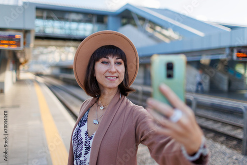 Pretty tourist takes a selfie at the train station. A girl in a hat and coat at the station. © zhukovvvlad