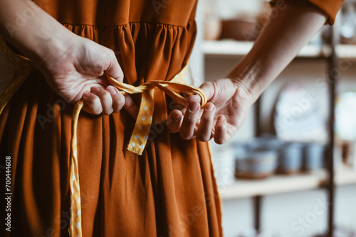 Fotografia Potter woman getting ready for work by putting on apron in workshop Hands of woman close-up tying apron, back view