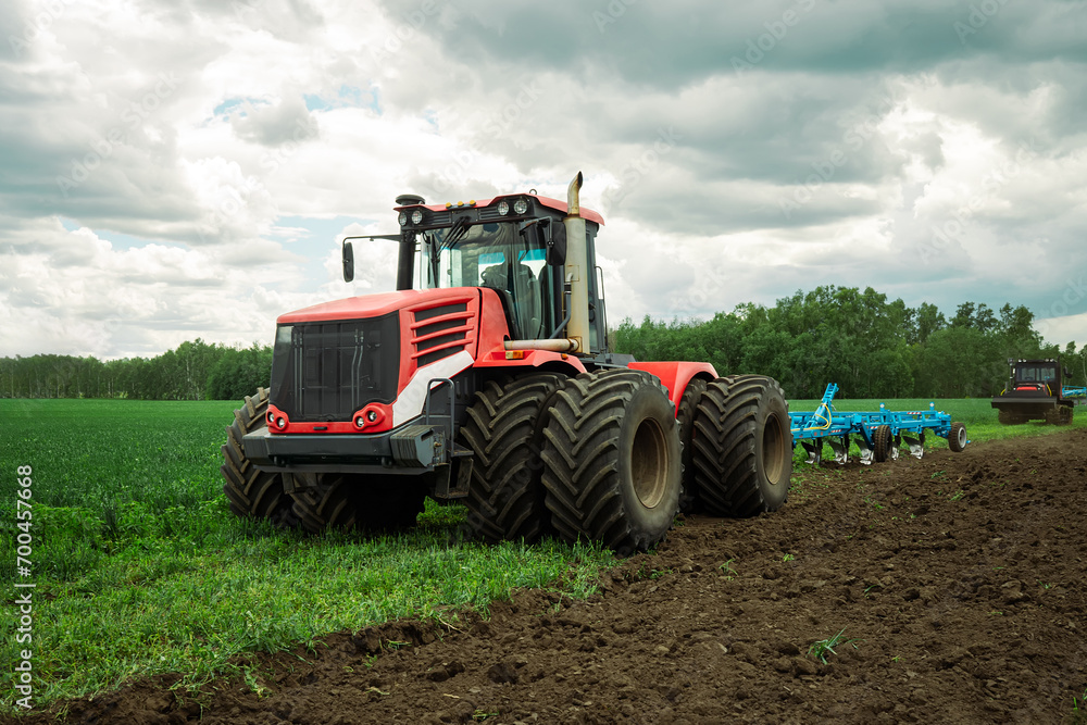 Red tractor working in a field on a bright sunny day. The concept of work in a fields and agriculture industry. Red tractor working in a field on a bright sunny day. The concept of work in a fields and agriculture industry.