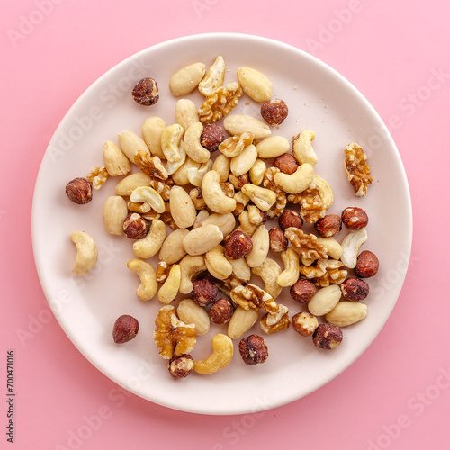 a variety of peeled nuts on a white plate, on a pink background