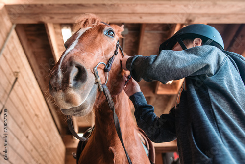 Low angle of young boy putting bridle on horse indoors photo
