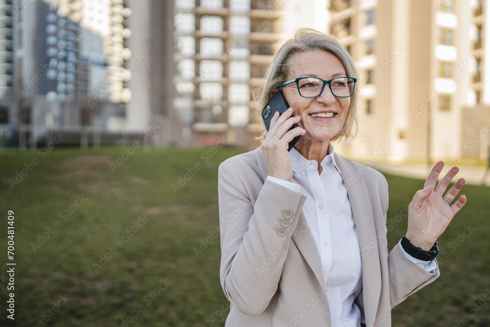 One mature woman outdoors in front of buildings talking on mobile phone, modern business and lifestyle concept One mature woman outdoors in front of buildings talking on mobile phone, modern business and lifestyle concept