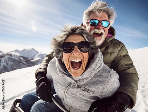 Happy senior couple having fun spending winter vacation in mountains sledding down the slope on a snowy mountain