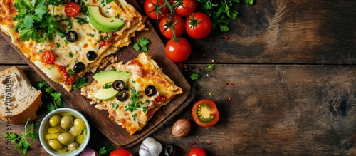 Healthy chicken and bean gluten free lasagna topped with pitted olives avocado tomatoes and fresh coriander in black baking dish on dark wood table vertical view. Creative Banner. Copyspace image photo