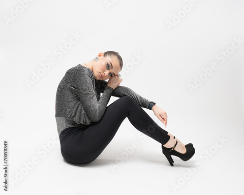 A young woman poses in a studio on a white background, sitting on the floor