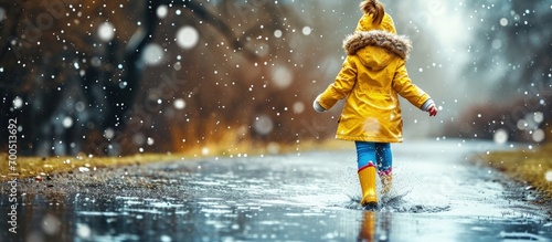 Close up of little toddler girl wearing yellow rain boots and walking during sleet on rainy cloudy day Cute child in colorful clothes jumping into puddle splashing with water outdoor activity photo