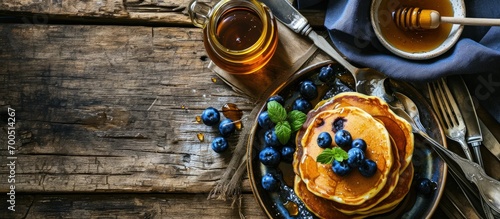 image shows a homemade fluffy pancake with blueberry on the top situation is decorated with rustiv wooden table placemat silver cutlery honey glass. Creative Banner. Copyspace image