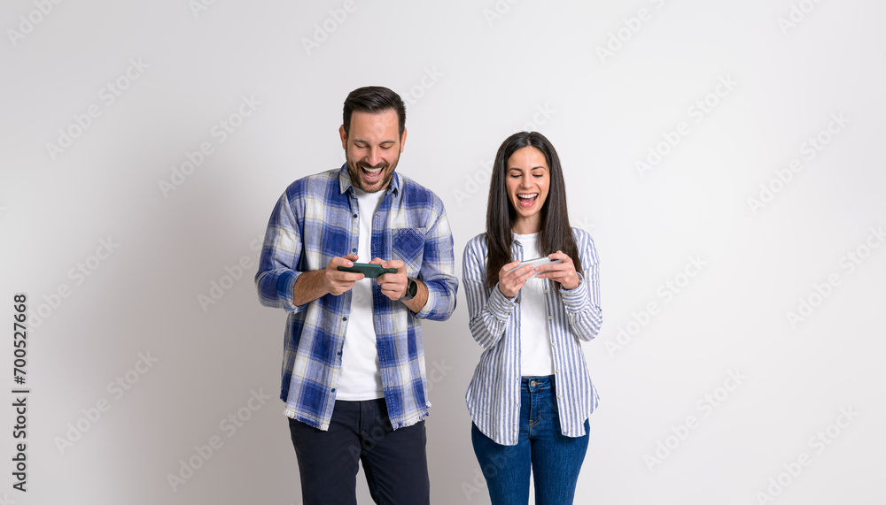 Cheerful young couple laughing and playing video games on mobile phones isolated over white background Cheerful young couple laughing and playing video games on mobile phones isolated over white background